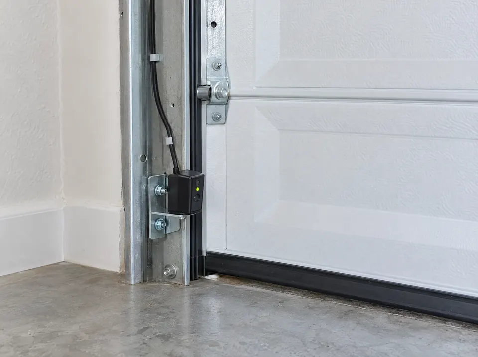 Garage door safety sensor mounted low on the track beside a closed white door