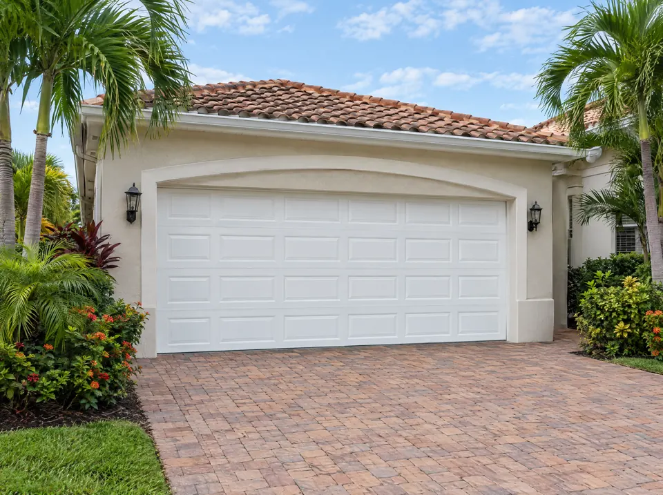 White two-car garage door on a stucco home with a tile roof and paver driveway